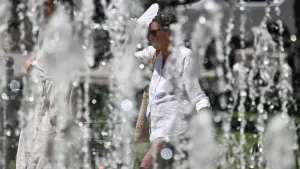 A woman shelters herself from the sun with a fan as she walks by a fountain during a heatwave in Sofia, Bulgaria on Monday. Hotel operators say European tourists may opt for…